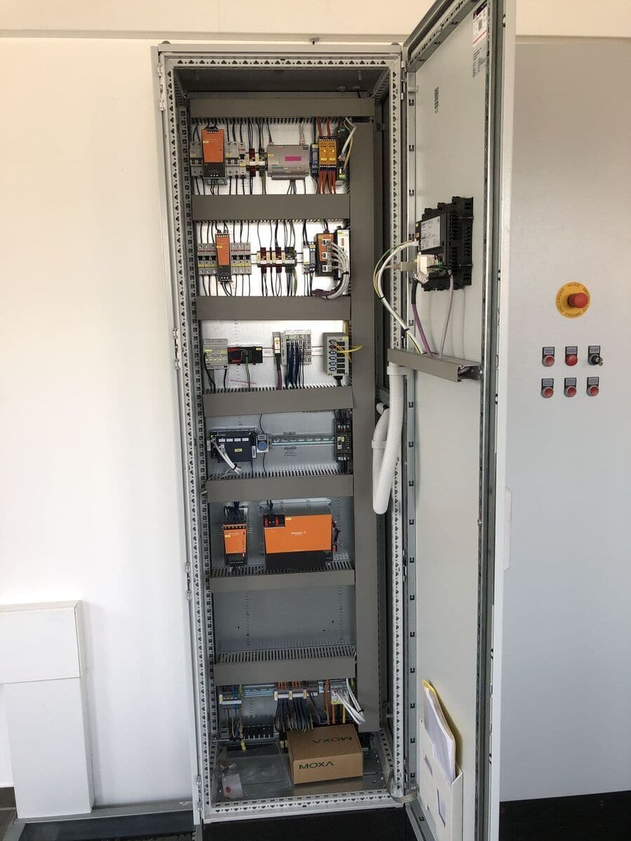 Ein geöffneter Schaltschrank mit elektronischen Komponenten und verkabelten Modulen in Grautönen.