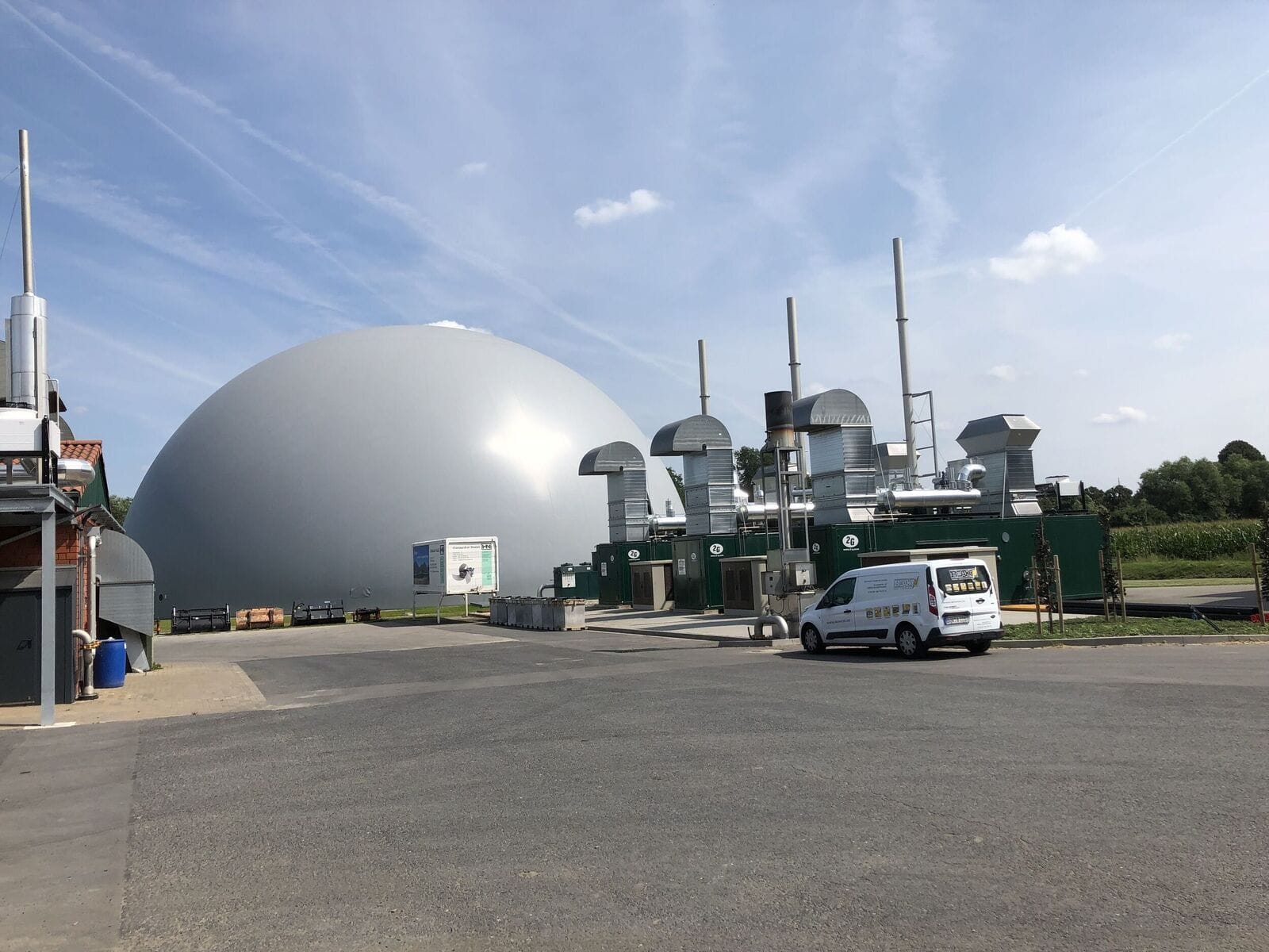 Industrielle Anlage mit grünem Gebäude und grauer Kuppel unter blauem Himmel.