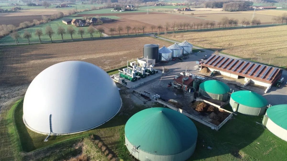 Biogasanlage mit weißen und grünen Kuppeln, umliegende Felder. Klarer Himmel, keine Personen sichtbar.